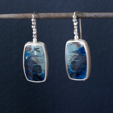Azurite earrings in brushed sterling silver with embellished ear wires, hanging on jeweller's file against a dark blue background