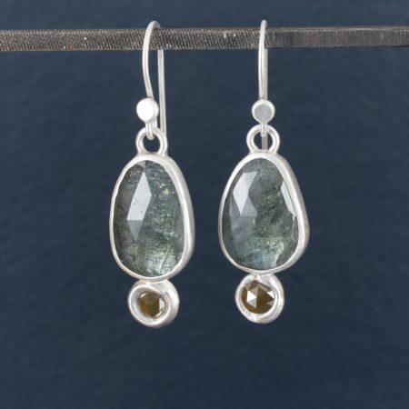 Moss aquamarine and diamond drop earrings hanging on jeweller's file