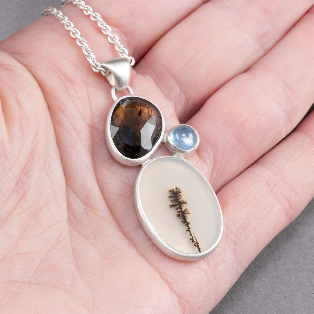 Dendritic agate, brown tourmaline and aquamarine pendant held in hand to show scale