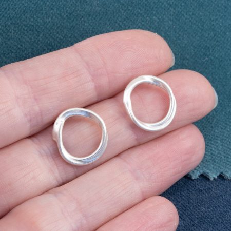 Tangled stud earrings in brushed sterling silver held in hand to show scale